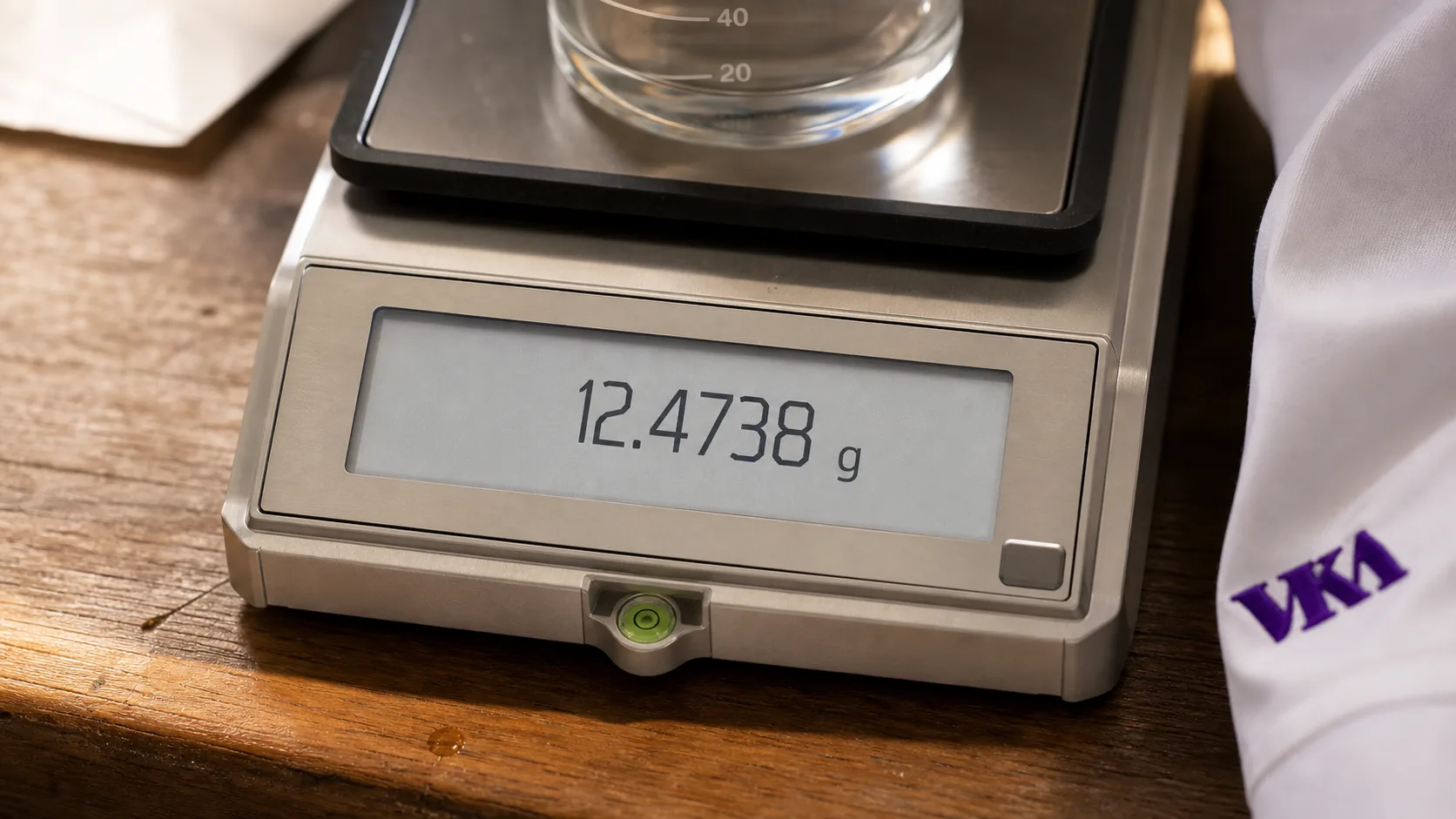 A flavourist part-way through a reformulation on the VKA Australia bench, weighing components against a balance readout while a recipe's nutrition figures change