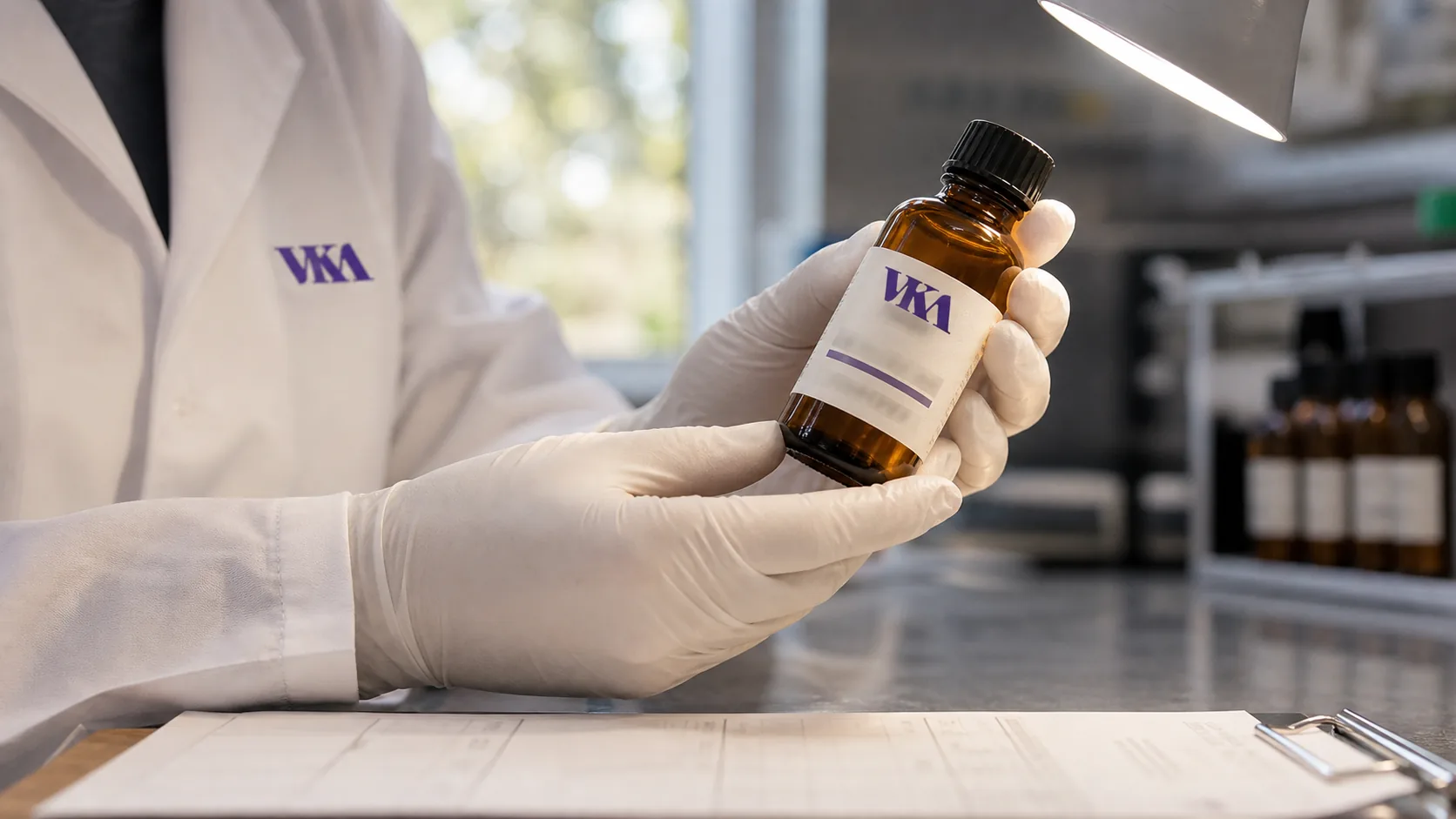 A QC operator checking a capped amber sample bottle under an inspection lamp at Southport.